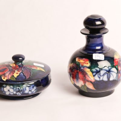 15   Moorcroft Pottery powder bottle with stopper and  covered  bowl. Orchid and Spring  Pattern. Dark blue ground.  5.5" H. Two pieces.  English.  Early 20th Century. 